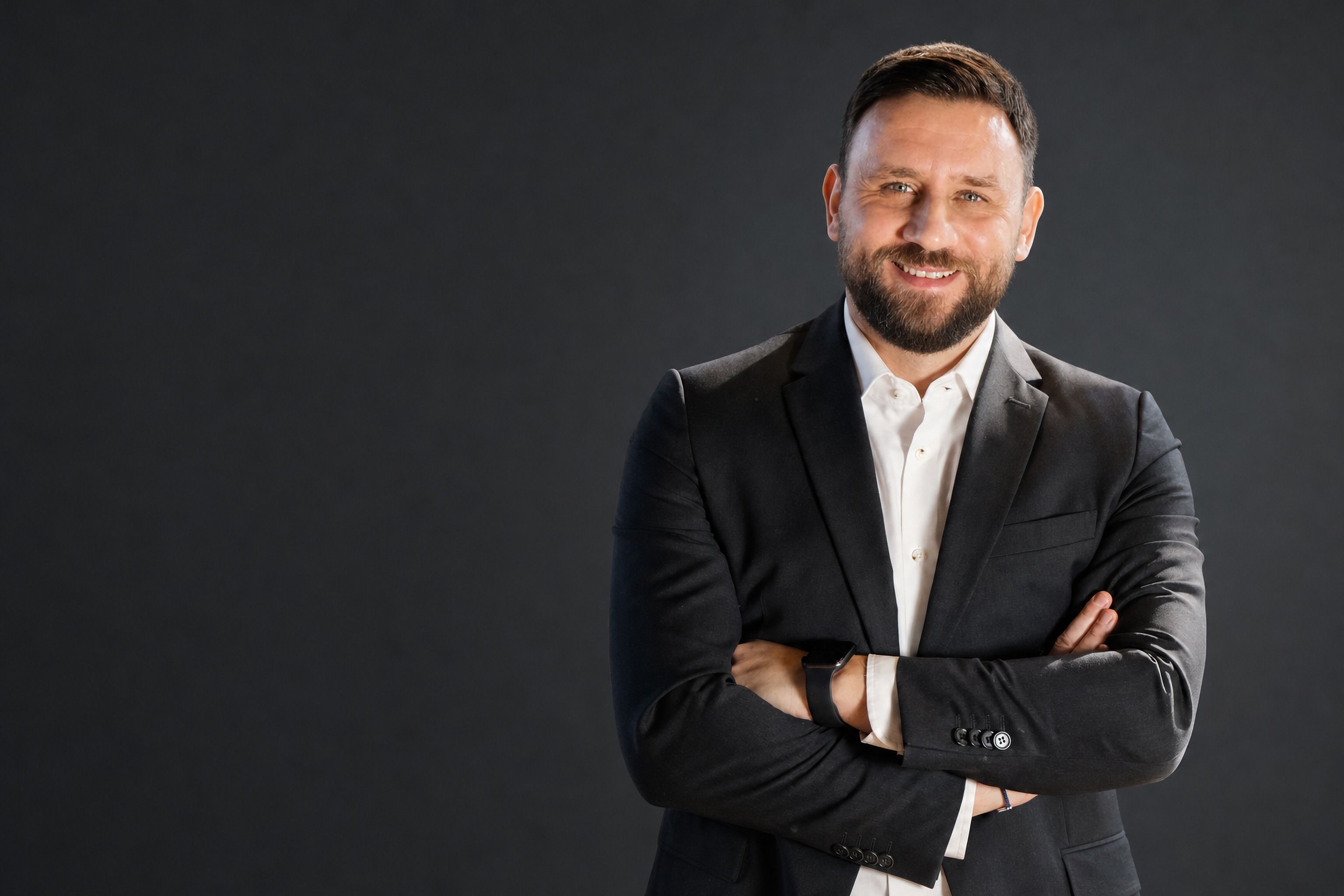 Ahmet Tolga Özol, koyu stüdyo fonu önünde kollarını kavuşturmuş, gülümsüyor